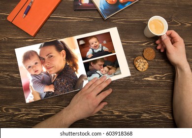 The Hand Man Holding A Family Photo Album  Against The Background Of The A Wooden Table
