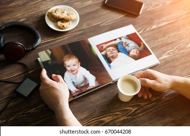 The Hand Man Holding A Family Photo Album  Against The Background Of The A Wooden Table
