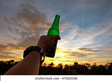 Hand Of Man Holding A Green Beer Bottle On The Sunset Sky