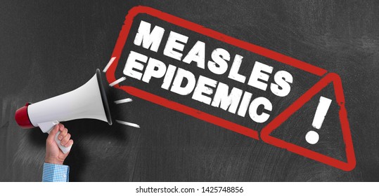 Hand Of Man Holding Megaphone Or Bullhorn Against Blackboard With MEASLES EPIDEMIC Warning Sign