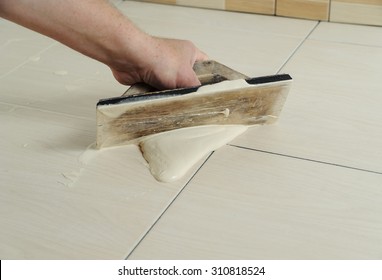 The hand of man holding a rubber float and filling joints with grout - Shutterstock ID 310818524
