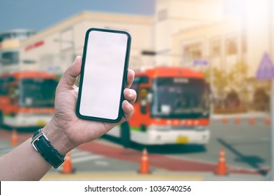 Hand man holding smartphone with blank white screen on blur image of bus station  background