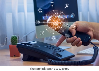 Hand Of Man Holding Telephone Handset And Pressing Button On Keypad, Office Desk With Cactus Pot, Computer Background, Ip Telephony Services Concept With Flying Icon And Connectivity