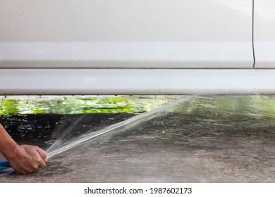 Hand Of A Man Holds The Blue Rubber Tube To Inject To Water Washing The Undercarriage Car In The Garage.