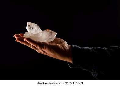 A Hand Of A Man Holds Two Huge Precious Quartz Crystals On A Black Background. Quartz Is A Mineral Composed Of Silica