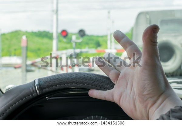 The hand of man inside the car. The car stopped in
front of a closed barrier and a red traffic light before the
railway crossing. Man outraged by the situation that did not have
time to ride the move