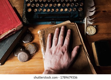 The Hand Of A Man Lies On The Old Book, An Old Working Office Desk Of Yesteryear, Reads An Oath