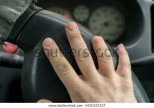 Hand of a man\
with a missing finger phalanx on the background of the steering\
wheel and dashboard of the\
car