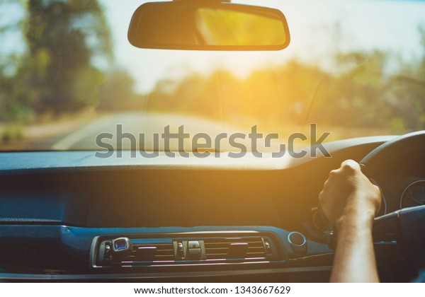 Hand of man on steering wheel drive a car\
with sunlight background.