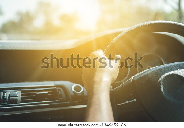 Hand of man on steering wheel drive a car\
with sunlight background.