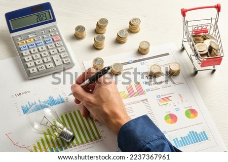 hand of a man with a pen on some electricity bills surrounded by coins a light bulb and a calculator