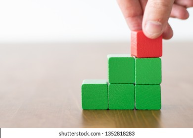 Hand Of A Man Picking Up A Red Wooden Cube On Top Of Stairs Of Green Stacked Cubes