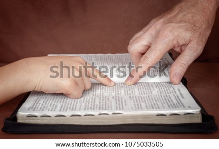 Hand of man pointing something to a child in the Bible book. Teaching a disciple from the Bible.