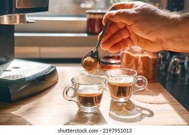 Hand of man putting brown sugar into cups with aromatic hot drink espresso, prepared in espresso coffee machine in the kitchen at home. Awakening drink. Morning habit. Selective focus. - Powered by Shutterstock