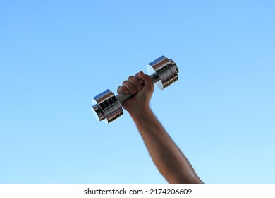 Hand Of A Man Show Us A Dumbbell Under A Blue Sky