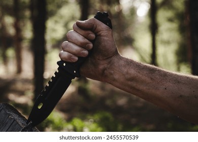 Hand of a man with a survival knife in his hands in the forest. Focus on the knife - Powered by Shutterstock