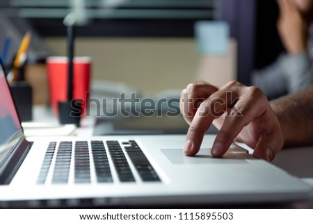 Hand of a man using laptop computer working overtime late at night in the office at his desk