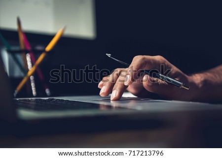 Hand of a man using laptop computer working overtime at his desk in the office late at night