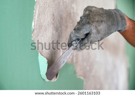 Hand of man using scraper or spatula to remove old paint wall for cleaning, repair, preparing concrete wall. Scraping to remove paint plaster peel.