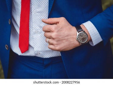 The hand of a man with a hand watch holds on to a blue suit against the background of a white shirt and red tie, a business men's style of clothing decor. - Powered by Shutterstock