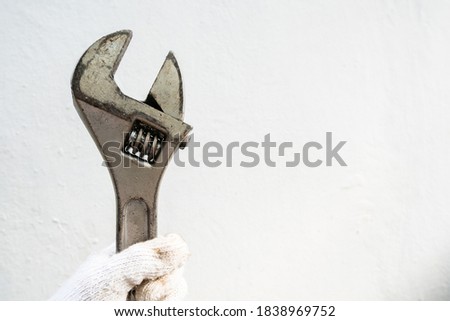 The hand of the man wearing gloves is holding an old wrench
