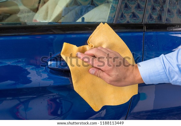 The hand of man\
wipes a car a yellow rag.