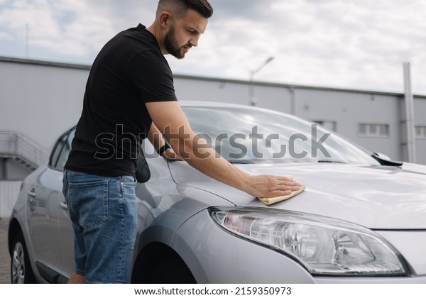 Hand of man wipes headlight of his car using rug.\
Self-service car wash.\
Outdoor