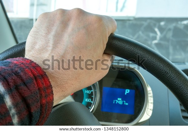 Hand of mans on the steering\
wheel, and Dashboard of the car, which stands still.\
Close-up.