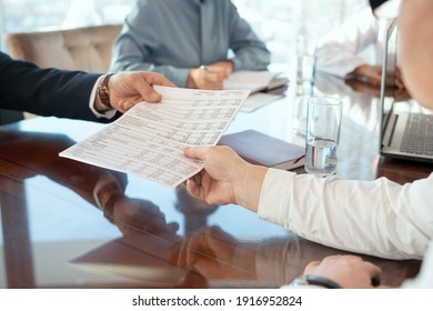 Hand of mature male delegate taking document with financial data being given by business partner against secretary making notes in notebook