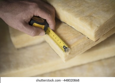 Hand measuring a fiberglass batt. Image of home insulation.