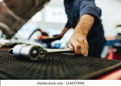 Hand of mechanic picking up a ratchet spanner from table in auto workshop. Mechanic working on garage with tools.