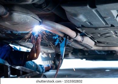 The Hand Of A Mechanic Or Welder Is Fixing A Car Exhaust System By Welding The Exhaust Pipe. Sparks Of Automobile Exhaust Pipe Welding. Auto Services. Selective Focus. Copy Space.