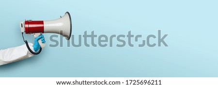 hand of medic or Nurse with gloves and a megaphone in front of an empty blue background, banner size, with copyspace for your individual text.