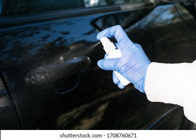 
hand in medical glove holds white bottle with a liquid antiseptic and sprays the jet to disinfect a car handle, protection against viruses, bacteria, coronavirus pandemic, healthcare concept