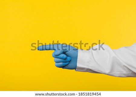 Hand in medical glove pointing finger on yellow paper background.