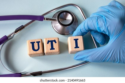 A hand in a medical glove puts cubes with the abbreviation UTI (Urinary Tract Infection) on the background of a stethoscope. Medical concept