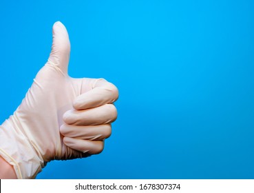 A hand in a medical rubber glove shows a thumbs up class, approval gesture on a blue background with copy space. The concept of defeating a disease or a good prognosis - Shutterstock ID 1678307374