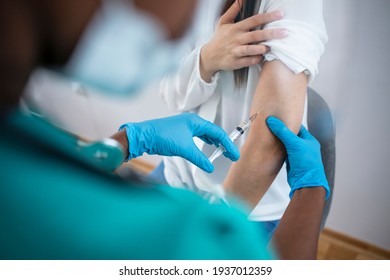 Hand of medical staff in blue glove injecting coronavirus covid-19 vaccine in vaccine syringe to arm muscle of woman for coronavirus covid-19 immunization. Female doctor  injecting a woman