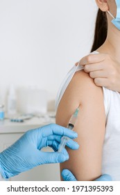 Hand of medical staff in blue glove injecting covid-19 vaccine to arm muscle of young woman for coronavirus immunization. - Shutterstock ID 1971395393