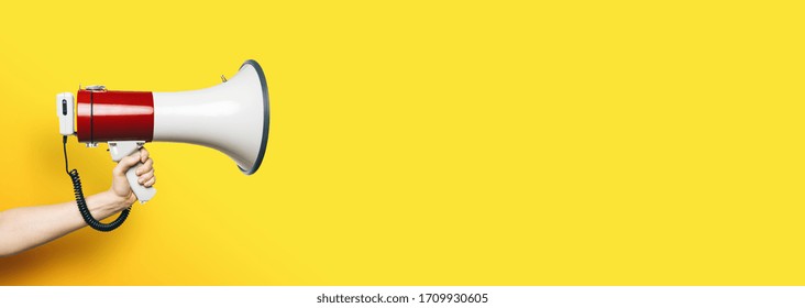 hand with a megaphone in front of an empty yellow background, banner size, with copyspace for your individual text. - Shutterstock ID 1709930605