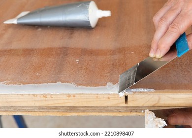 Hand With Metal Putty Knife And Glass Putty Restores The Bottom Of The Wooden Door.