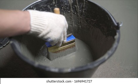 Hand mixes waterproofing mortar in a bucket. Male hand holding a brush to apply waterproofing to the floor. Waterproofing solution in a bucket.