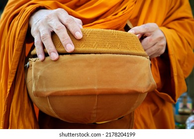 hand of monk dressing orange robe, holding bowl during reception of alms, around buddhist temple