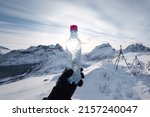 Hand of mountaineer holding water bottle on snow covered mountain peak in the morning