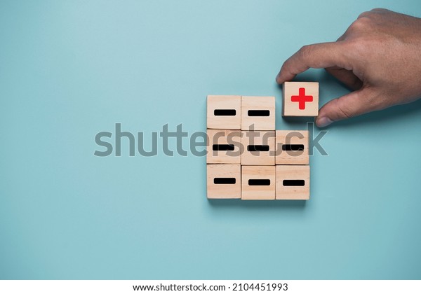 Hand move red plus sign move out from\
black minus sign which print screen on wooden cube on blue\
background for positive thinking and mindset\
concept.