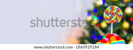 hand in multi-colored glove holds a lollipop against the background of the Christmas tree. Panoramic 
