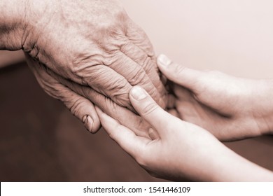 The hand of an old grandmother holds the hand of a child. Concept of help, care, support.