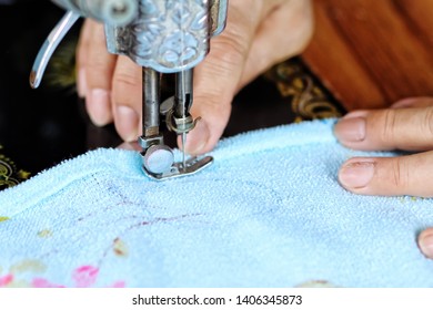 hand of a old lady sewing a blue clothes using sewing machine.