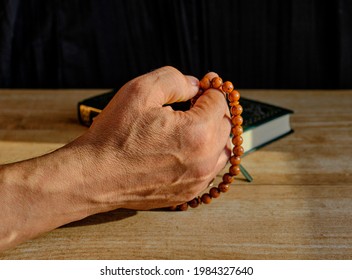 Hand Of A Older Muslim Man Fingering A Rosary Made Of Stone On A Background Of A Book Of Quran. Close Up Copy Space