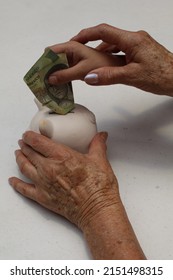 Hand Of An Older Woman Holding A Piggy Bank And Hand Of A Girl Depositing Mexican Money